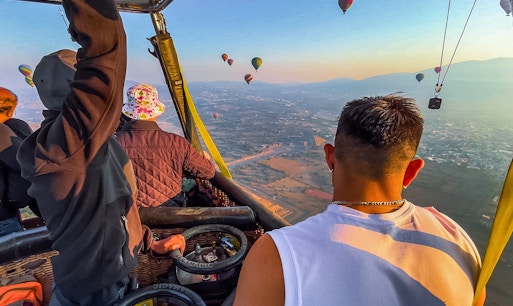 Passengers in a hot air balloon over Teotihuacan pyramids, Mexico, with other balloons in the sky.