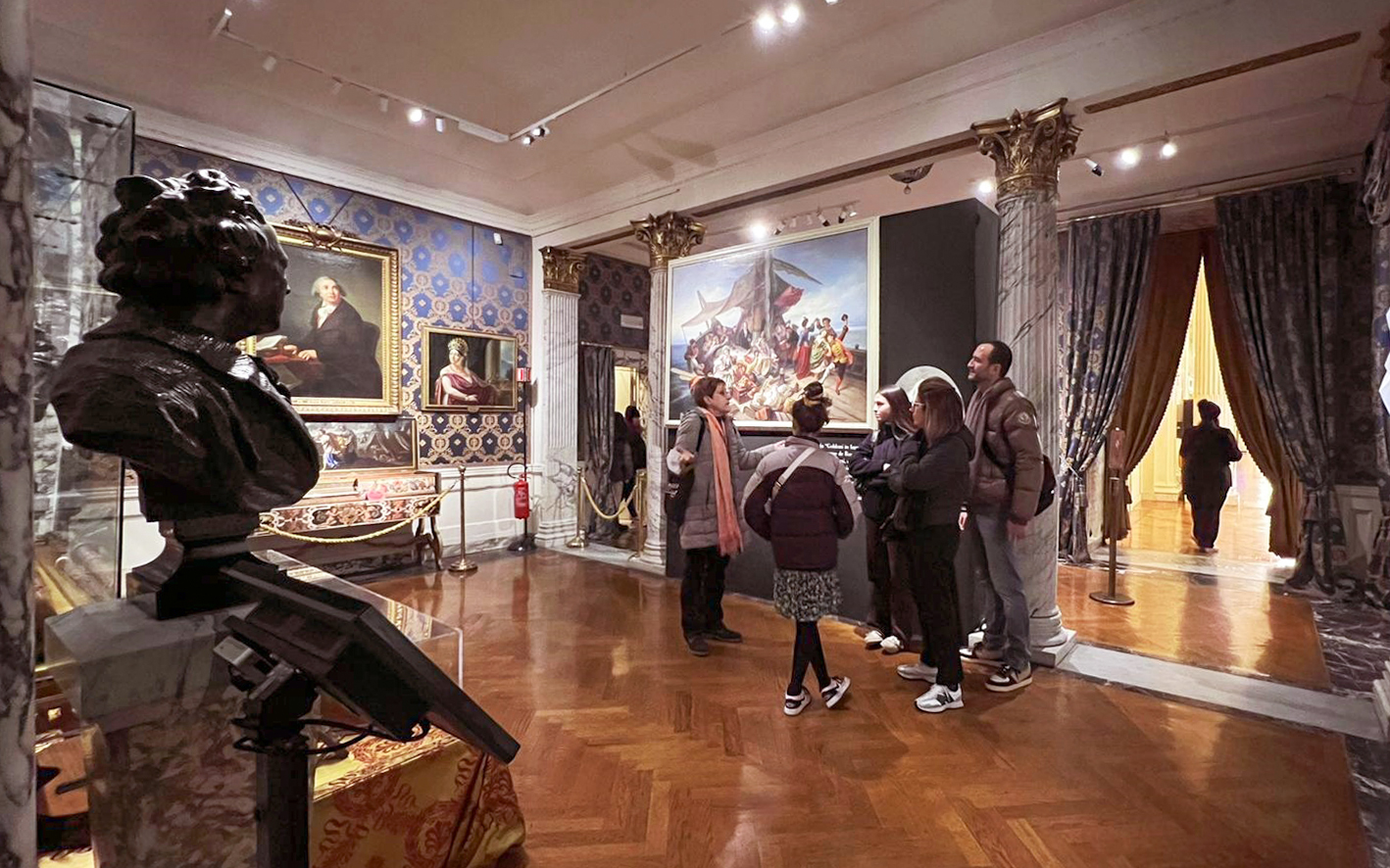Guide explaining artwork to tourists inside La Scala Theatre museum room.