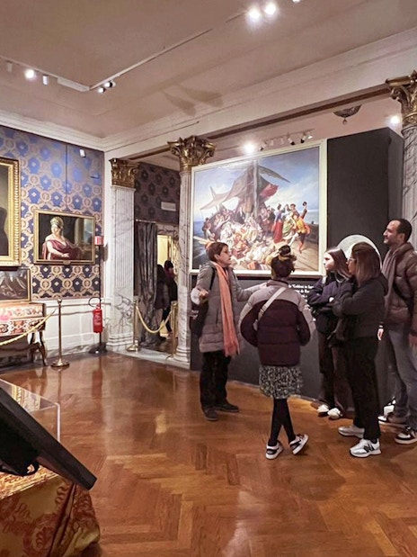Guide explaining artwork to tourists inside La Scala Theatre museum room.