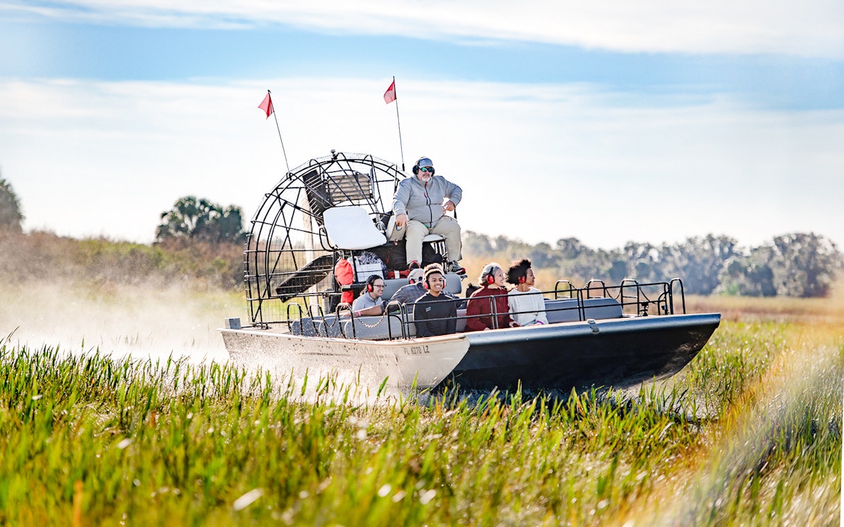 Airboat with tourists gliding through marshes on Boggy Creek Airboat Tour, Orlando.
