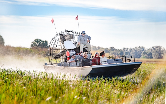 Airboat with tourists gliding through marshes on Boggy Creek Airboat Tour, Orlando.