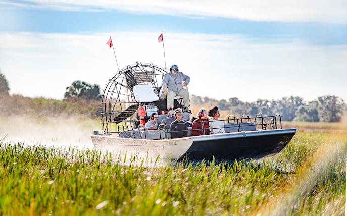 Airboat with tourists gliding through marshes on Boggy Creek Airboat Tour, Orlando.