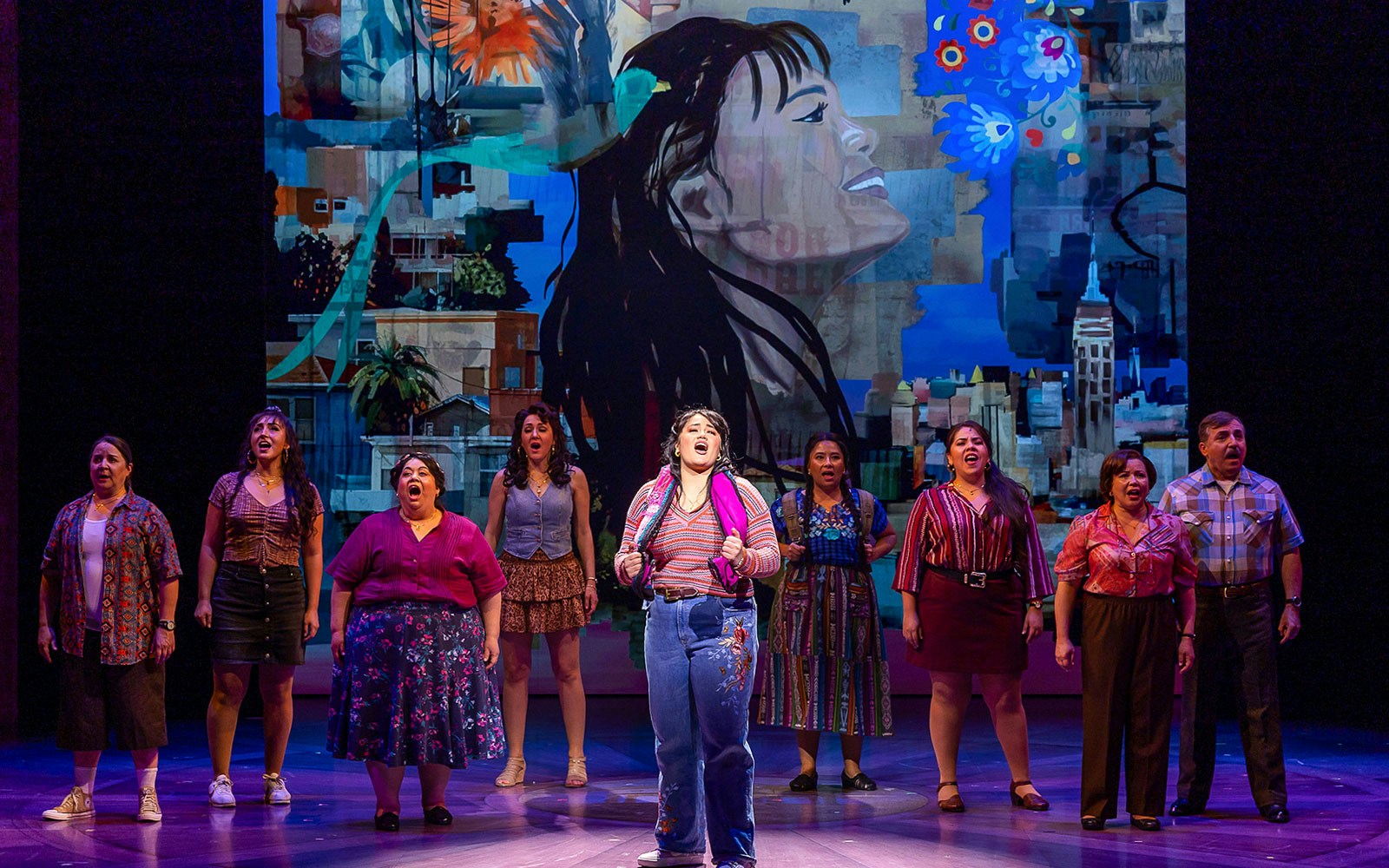 Performers singing on stage in "Real Women Have Curves: The Musical" with vibrant backdrop.