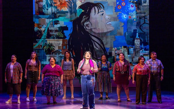 Performers singing on stage in "Real Women Have Curves: The Musical" with vibrant backdrop.