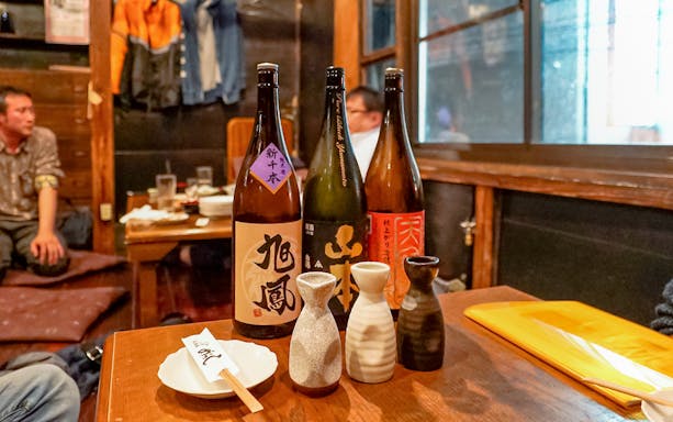 Sake bottles and cups on a wooden table in a cozy Japanese bar interior.