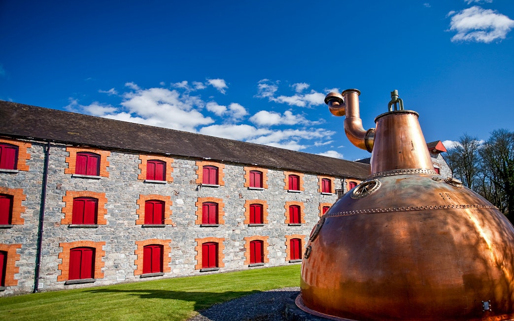 Midleton Distillery exterior with copper pot still and stone building with red shutters.