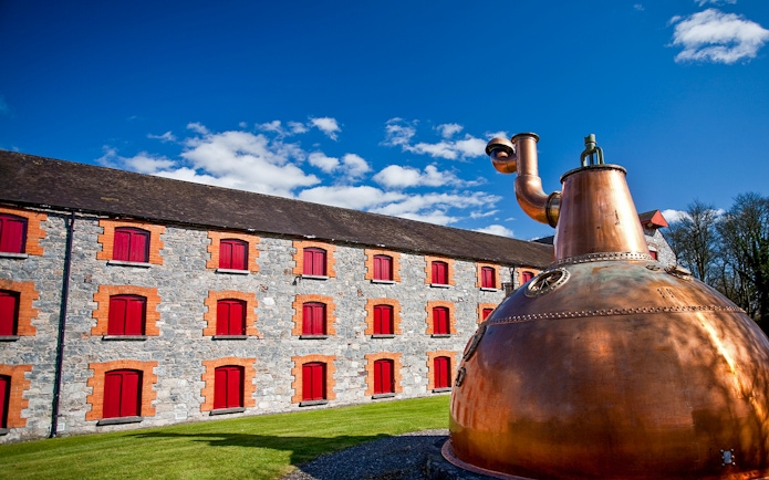 Midleton Distillery exterior with copper pot still and stone building with red shutters.