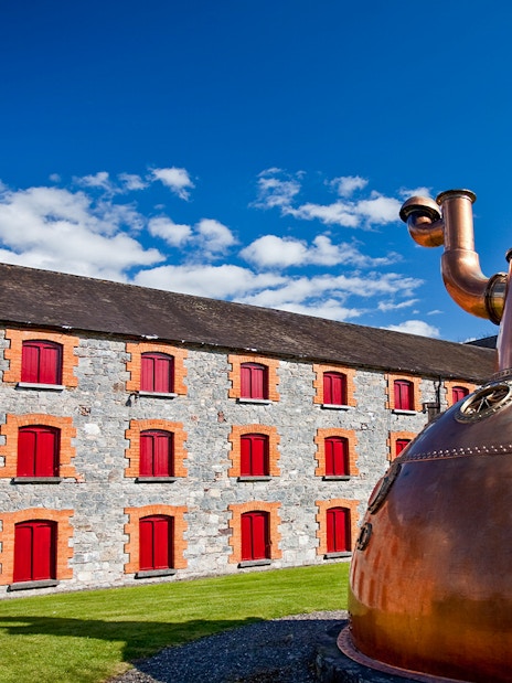 Midleton Distillery exterior with copper pot still and stone building with red shutters.