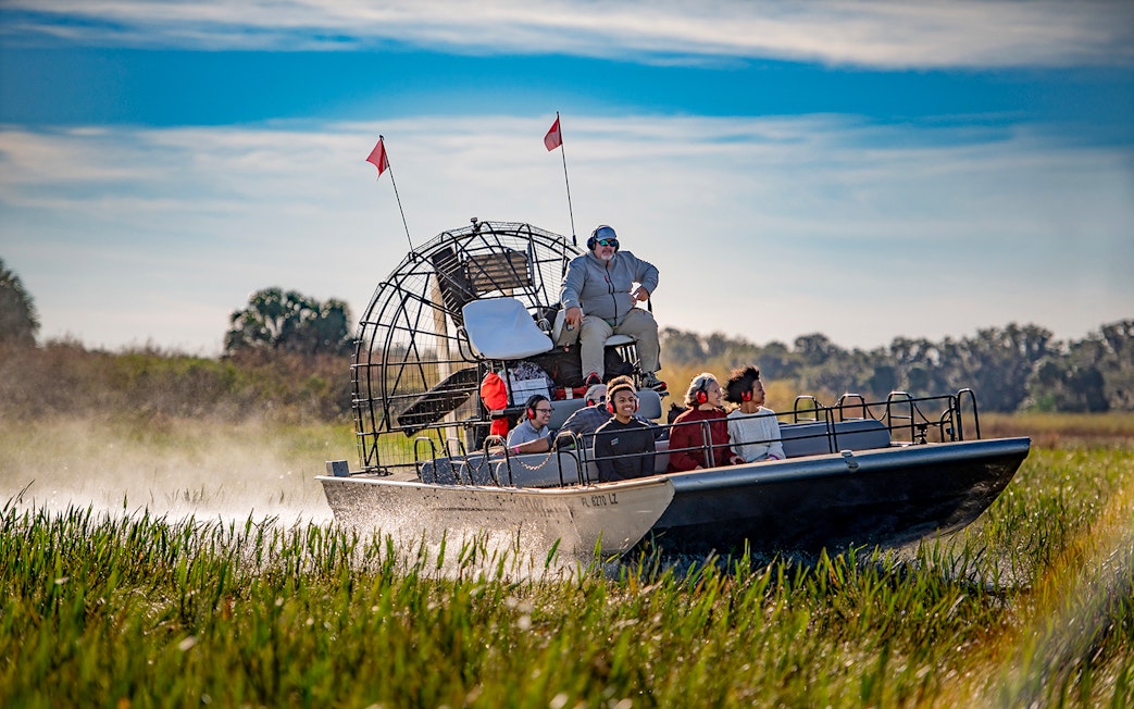 Guests on an airboat tour at Boggy Creek, Florida, gliding through marshlands.