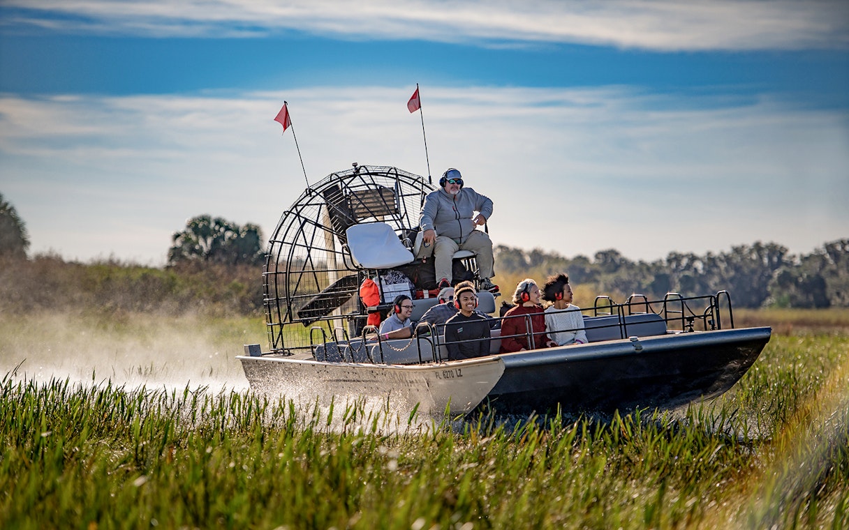 Guests on an airboat tour at Boggy Creek, Florida, gliding through marshlands.