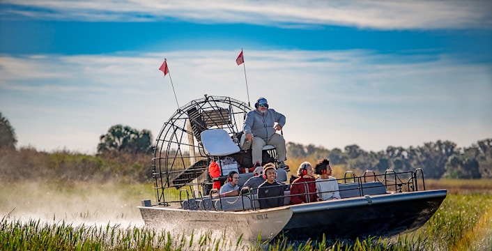 Guests on an airboat tour at Boggy Creek, Florida, gliding through marshlands.
