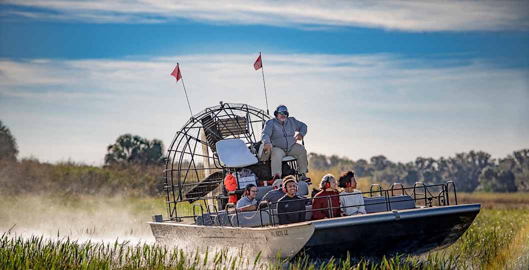 Guests on an airboat tour at Boggy Creek, Florida, gliding through marshlands.