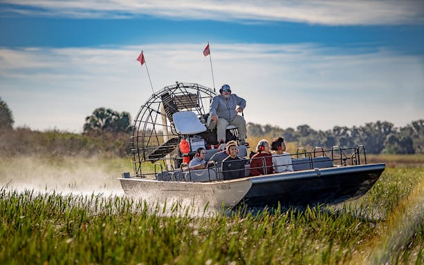 Guests on an airboat tour at Boggy Creek, Florida, gliding through marshlands.