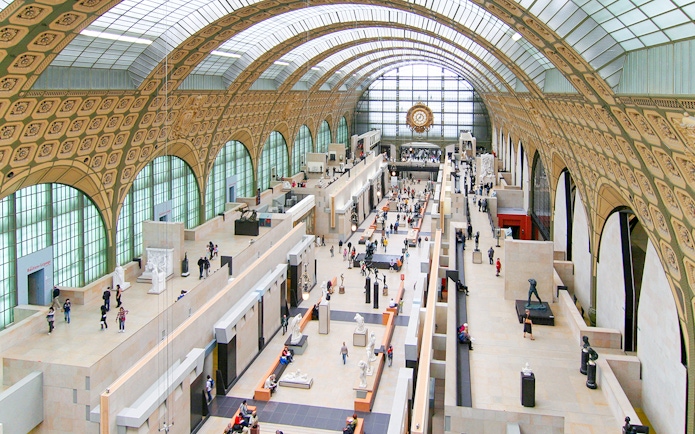 Main hall of the d'Orsay Museum in Paris, showcasing sculptures and visitors.