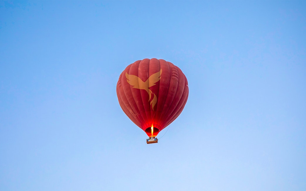 Hot air balloon in flight over Ras Al Khaimah against clear blue sky.