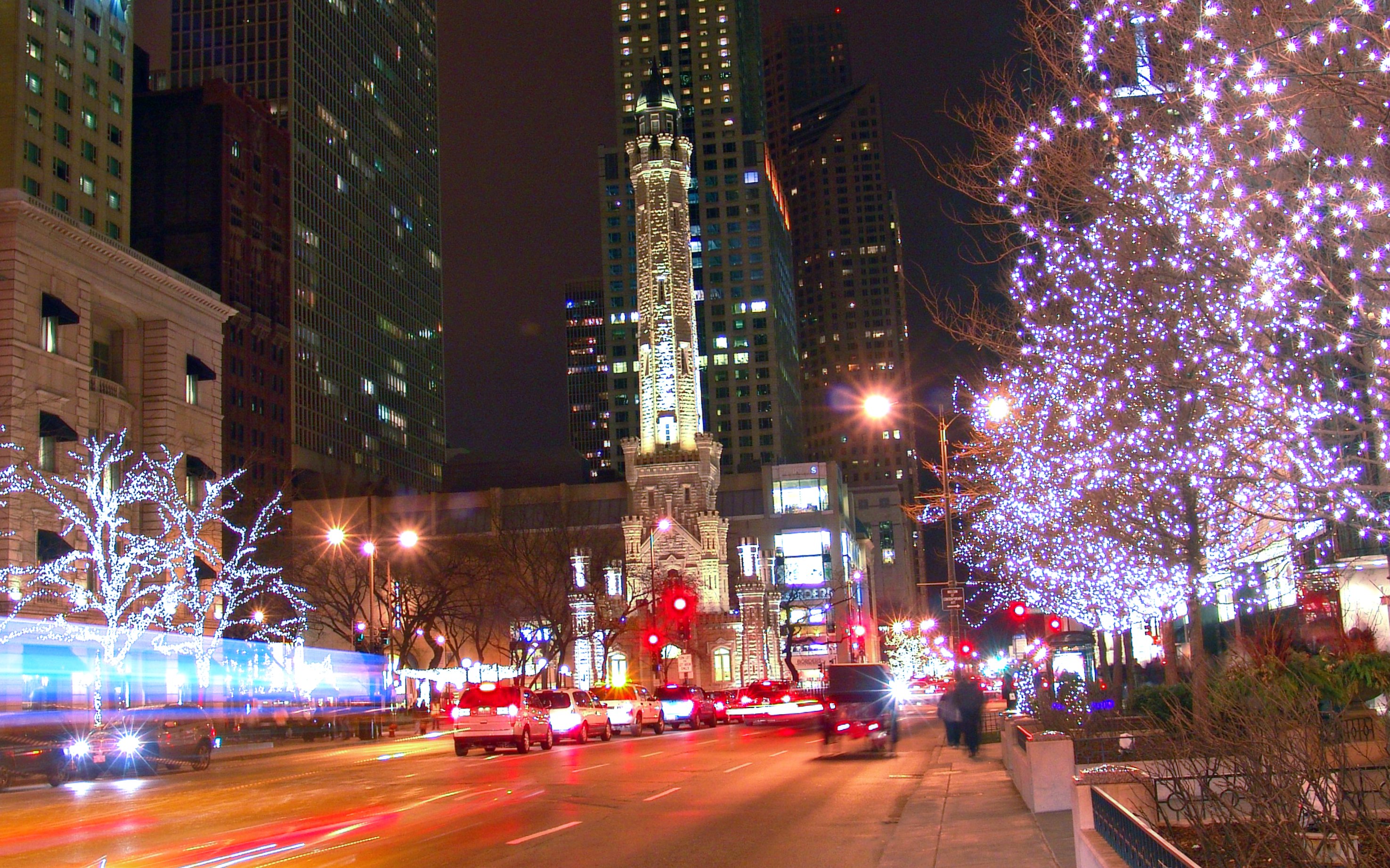 Chicago Water Tower at night with festive Christmas lights and bustling street traffic.