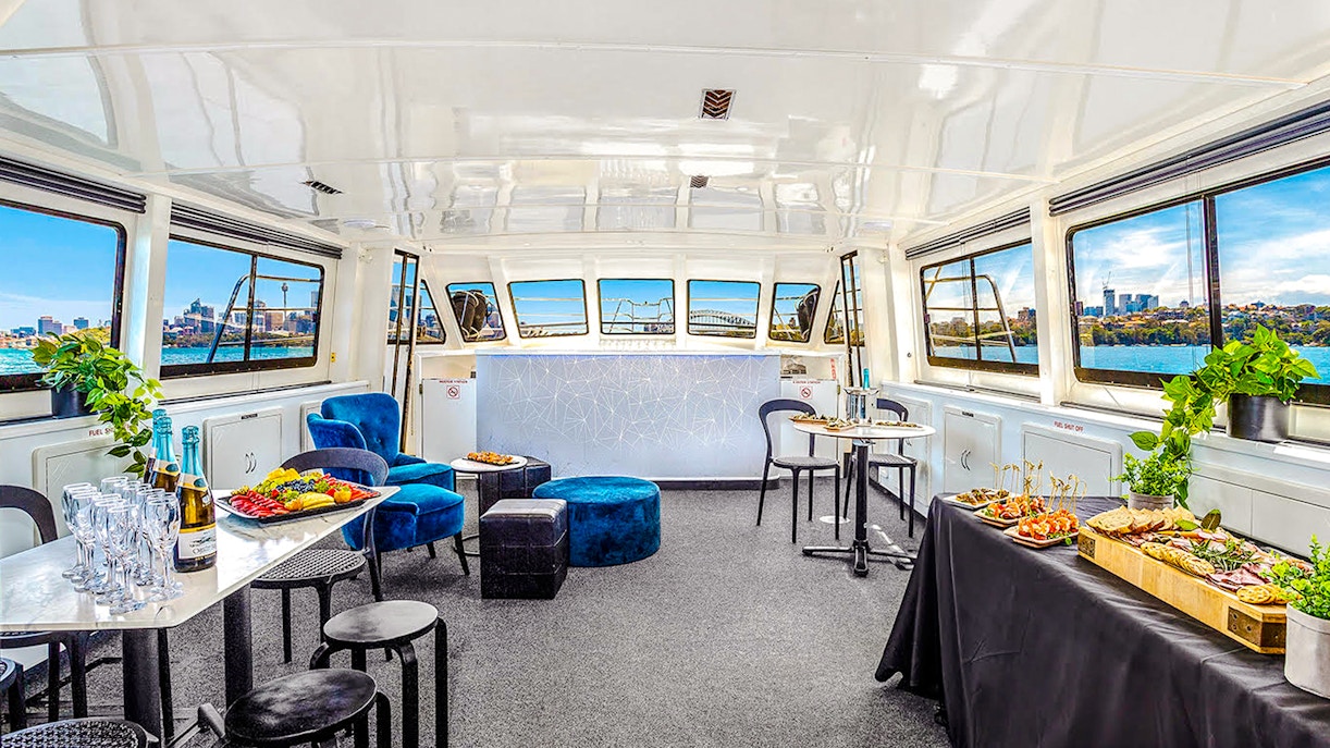 Interior of a boat set for a Golden Glow sunset harbour cruise in Sydney, featuring tables with food and drinks.