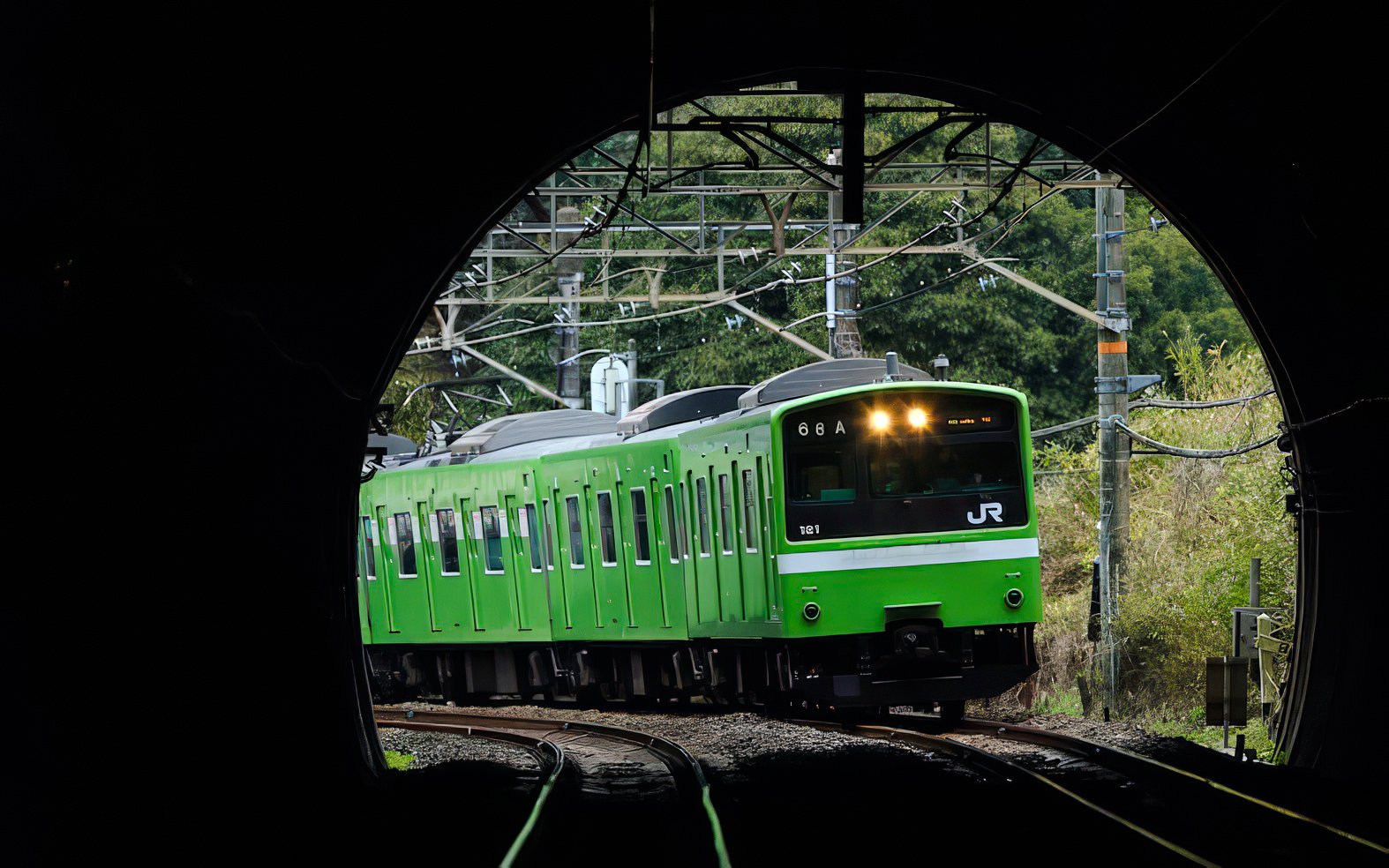 Green JR train emerging from tunnel in Kansai region, Japan.