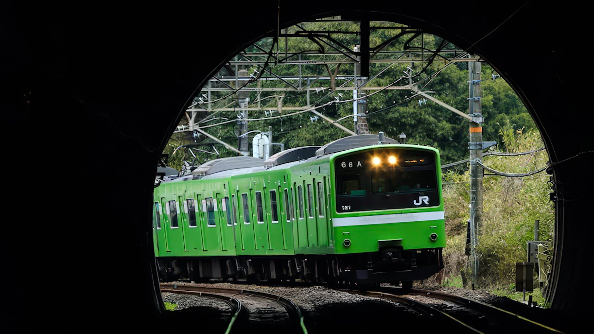 Green JR train emerging from tunnel in Kansai region, Japan.