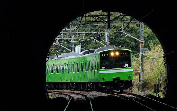 Green JR train emerging from tunnel in Kansai region, Japan.