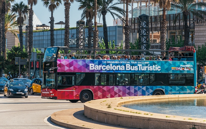 Barcelona hop-on hop-off tour bus near palm trees and city buildings.