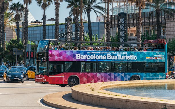 Barcelona hop-on hop-off tour bus near palm trees and city buildings.