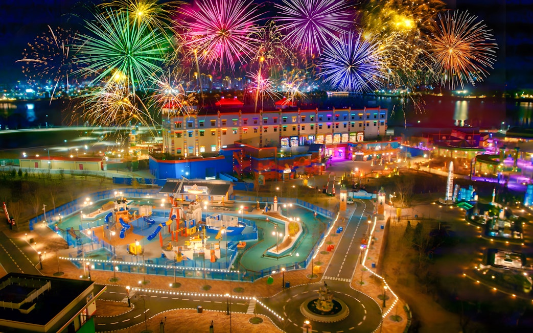Fireworks display over Legoland theme park at night, showcasing colorful attractions and vibrant lights.