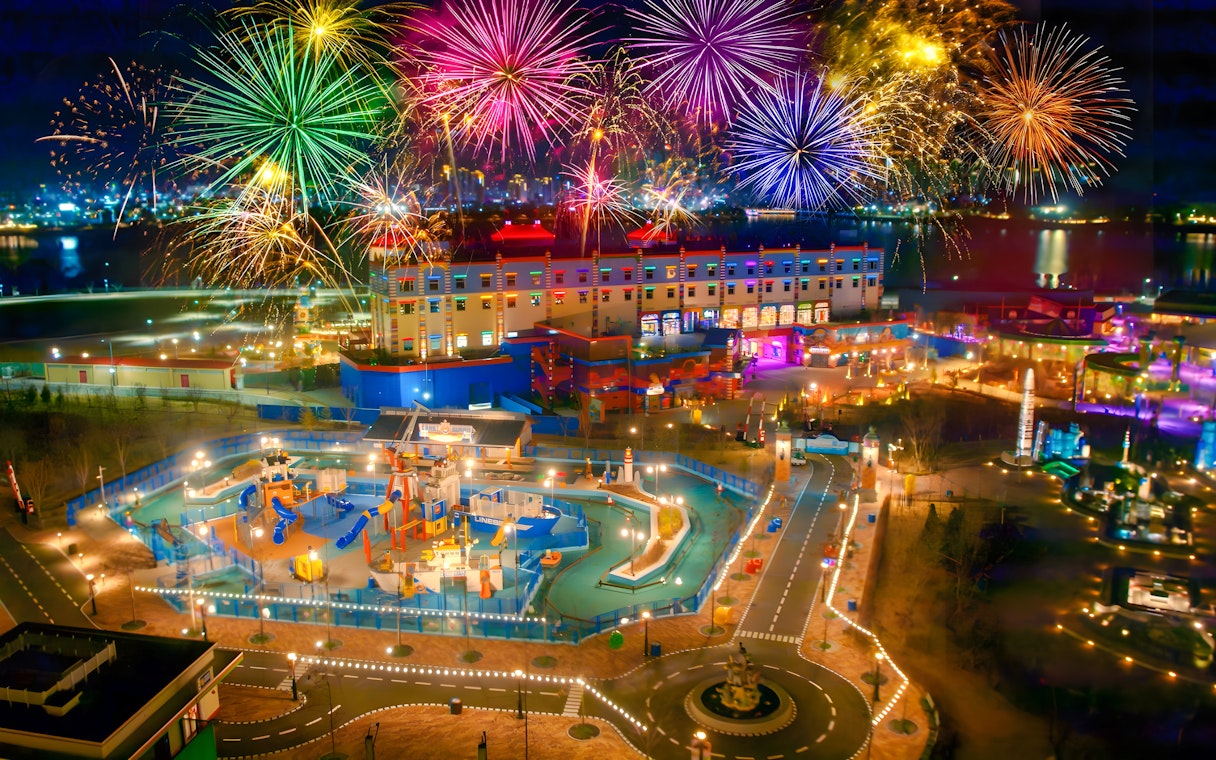 Fireworks display over Legoland theme park at night, showcasing colorful attractions and vibrant lights.