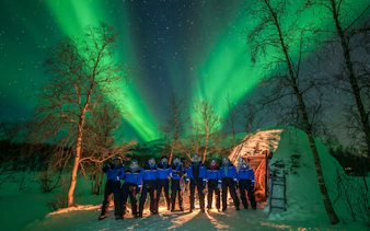Group in winter gear under Northern Lights in Abisko, Sweden.