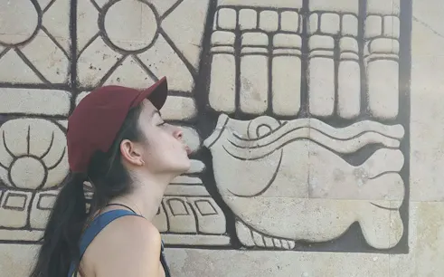 Woman interacting with ancient Mayan stone carving in Mérida during self-guided city exploration game.