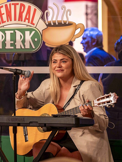 Musician playing guitar at Central Perk set during The FRIENDS™ Experience.