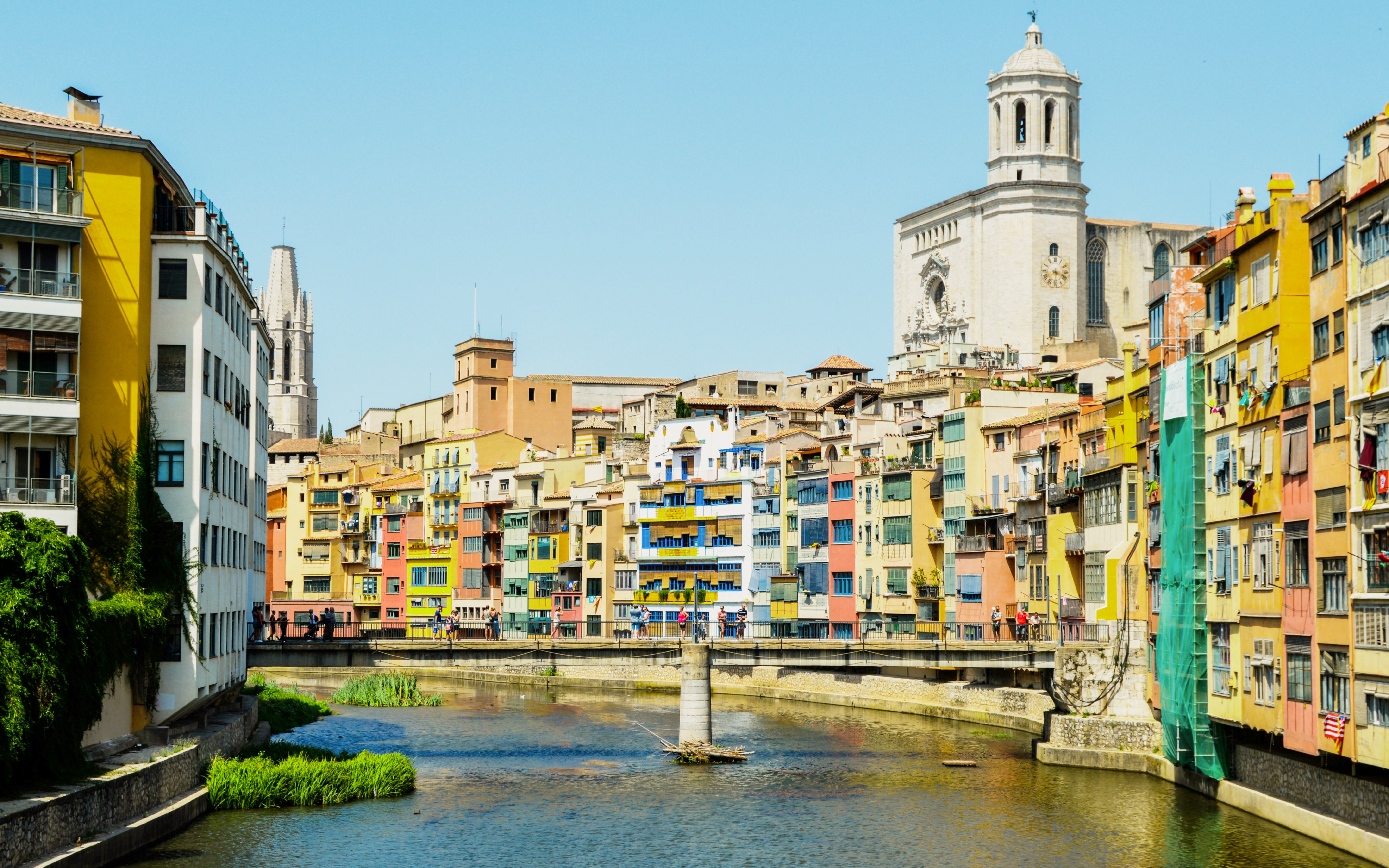 Colorful houses along the Onyar River in Girona, Spain with a cathedral in the background.
