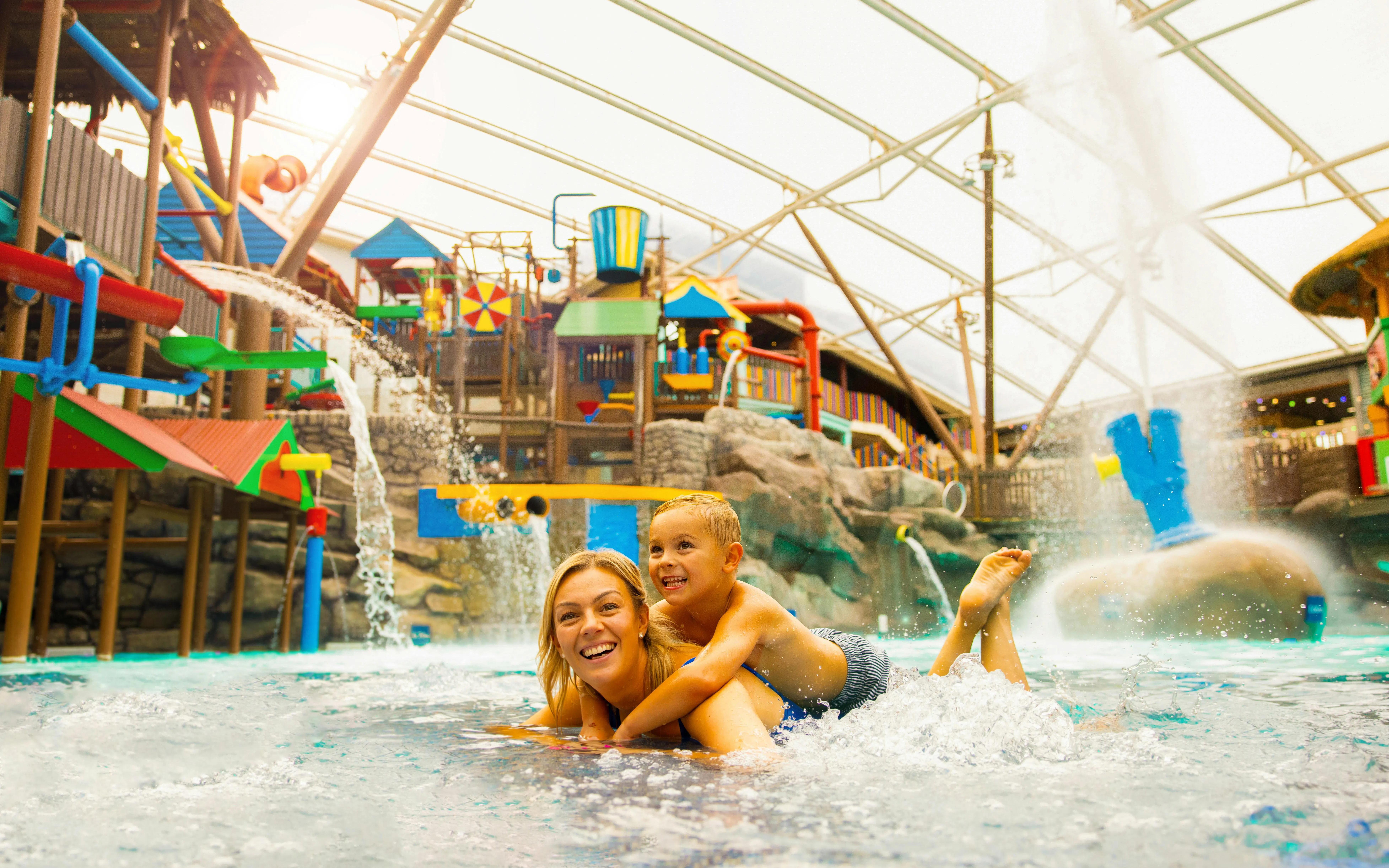 Child riding on adult's back in Alton Towers Waterpark with colorful slides and water features.