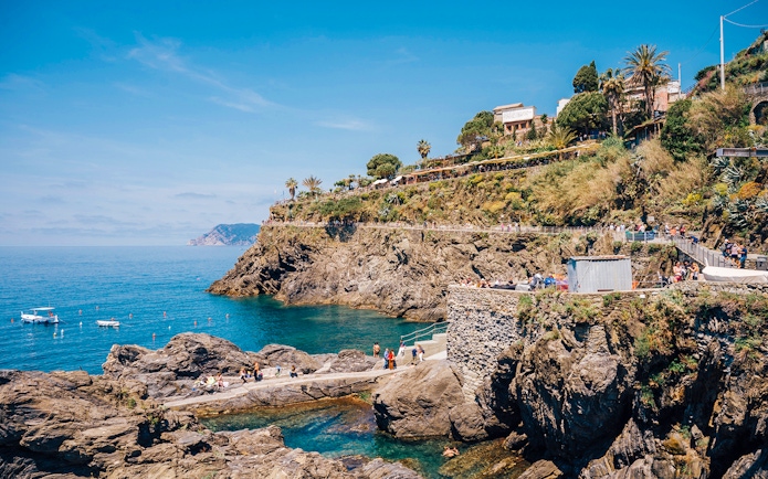 Cinque Terre coastline with rocky cliffs and people walking along the path, Italy.