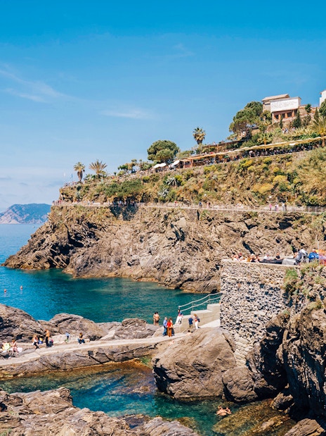 Cinque Terre coastline with rocky cliffs and people walking along the path, Italy.