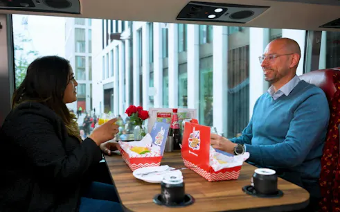 Passengers enjoying fish and chips with drinks on a London sightseeing bus tour.