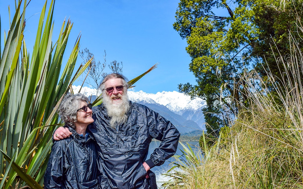 Tourists enjoying a rainforest walk at Franz Josef with snowy mountains in the background.
