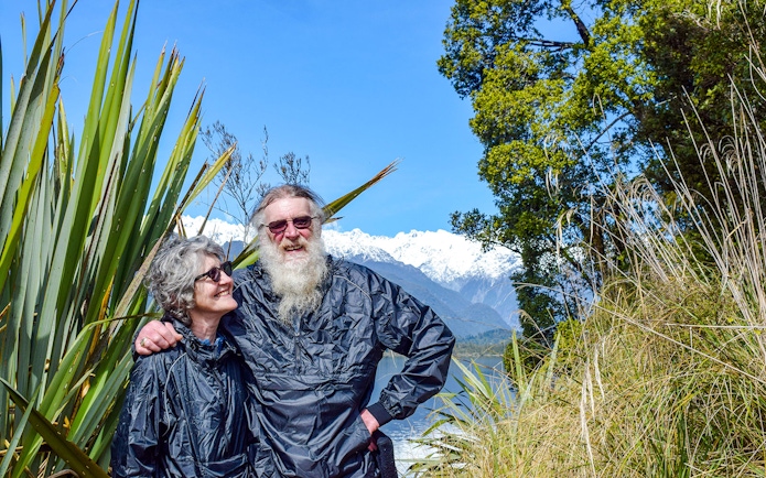 Tourists enjoying a rainforest walk at Franz Josef with snowy mountains in the background.