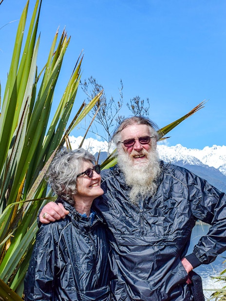 Tourists enjoying a rainforest walk at Franz Josef with snowy mountains in the background.