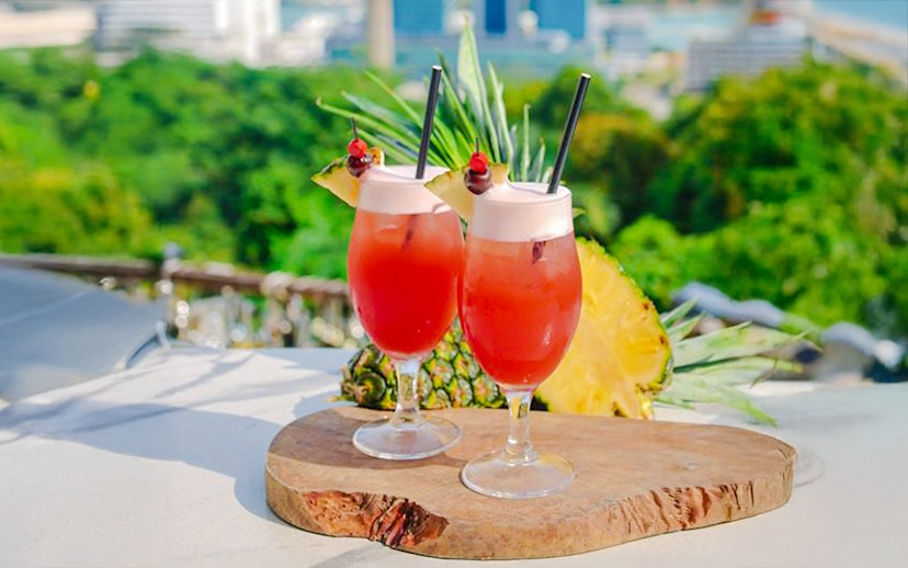Singapore Sling cocktails on a table at Mount Faber with a view of lush greenery.