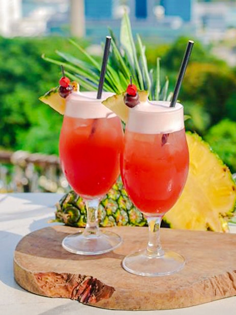 Singapore Sling cocktails on a table at Mount Faber with a view of lush greenery.