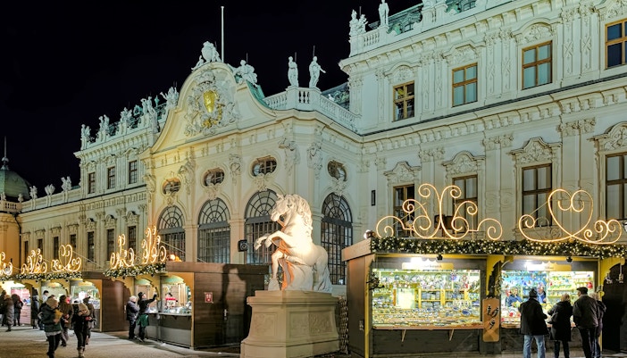 Christmas market stalls in front of the illuminated Upper Belvedere Palace, Vienna, Austria.