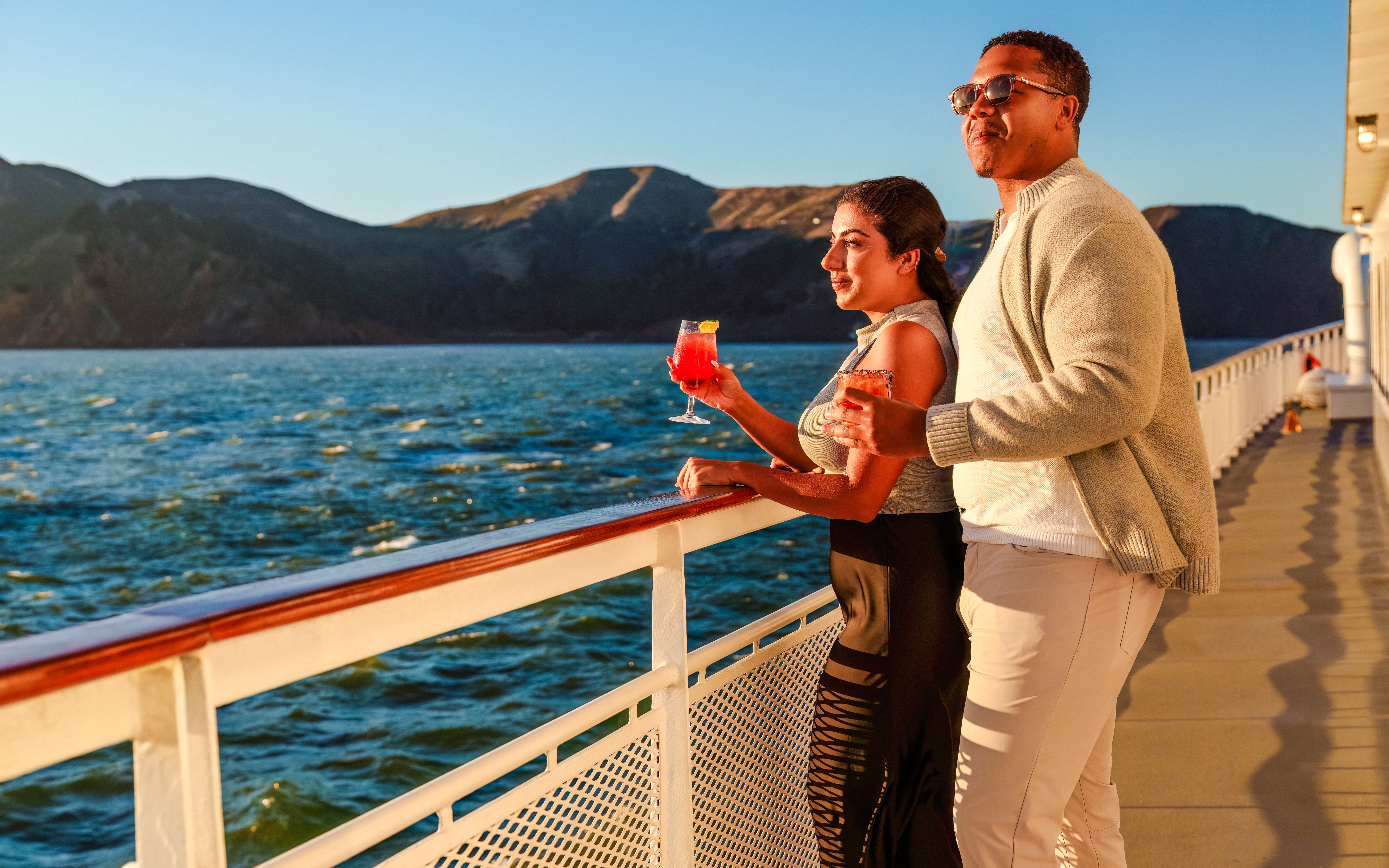 Couple enjoying drinks on a San Francisco dinner cruise deck at sunset.