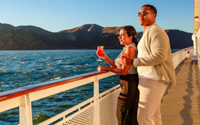 Couple enjoying drinks on a San Francisco dinner cruise deck at sunset.