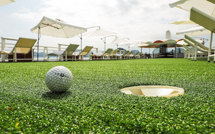 Golf ball near hole on deck of Starlight Cruise with lounge chairs and umbrellas.