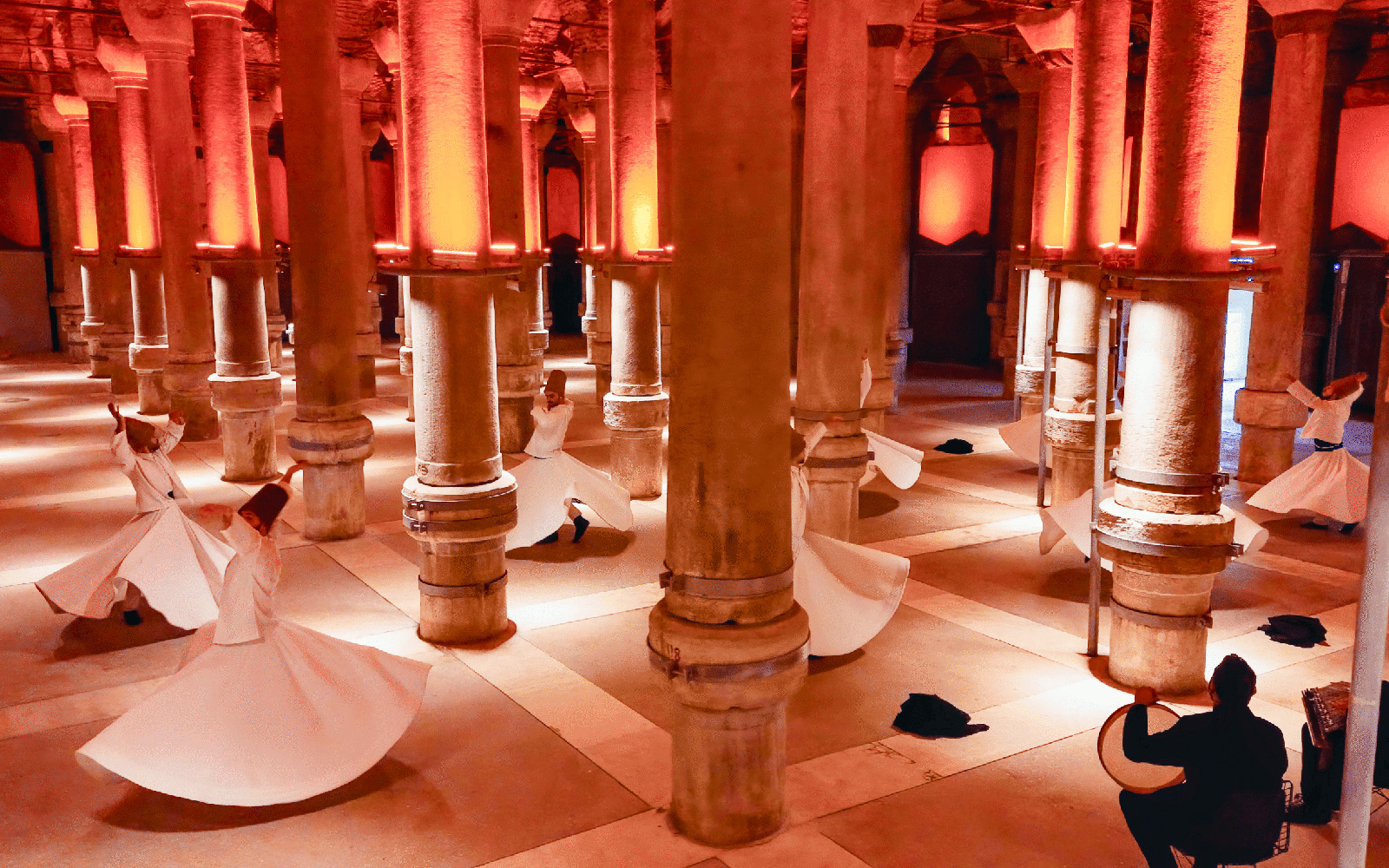 Whirling Dervishes performing in a historic Istanbul venue with stone columns.