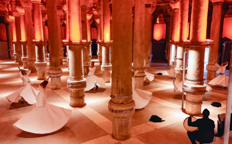 Whirling Dervishes performing in a historic Istanbul venue with stone columns.