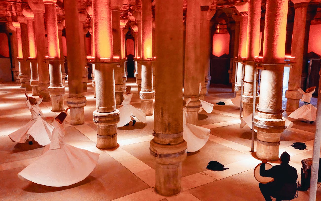 Whirling Dervishes performing in a historic Istanbul venue with stone columns.
