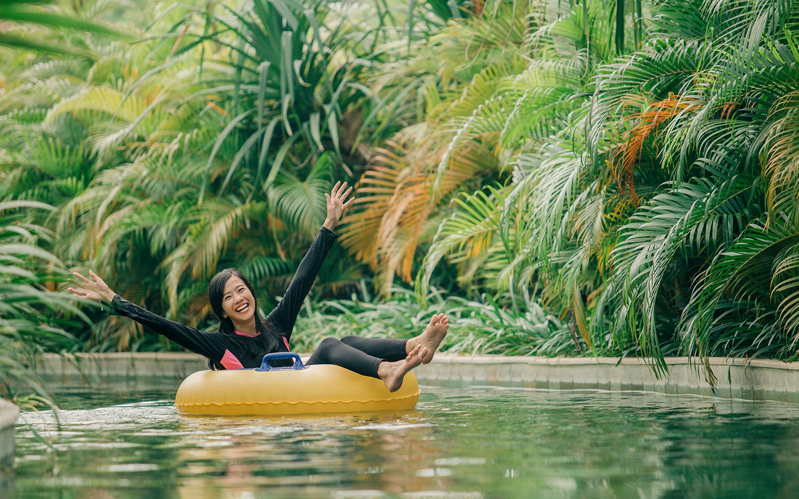 Girl floating on a ring in lazy river at Waterbom Bali surrounded by lush greenery.