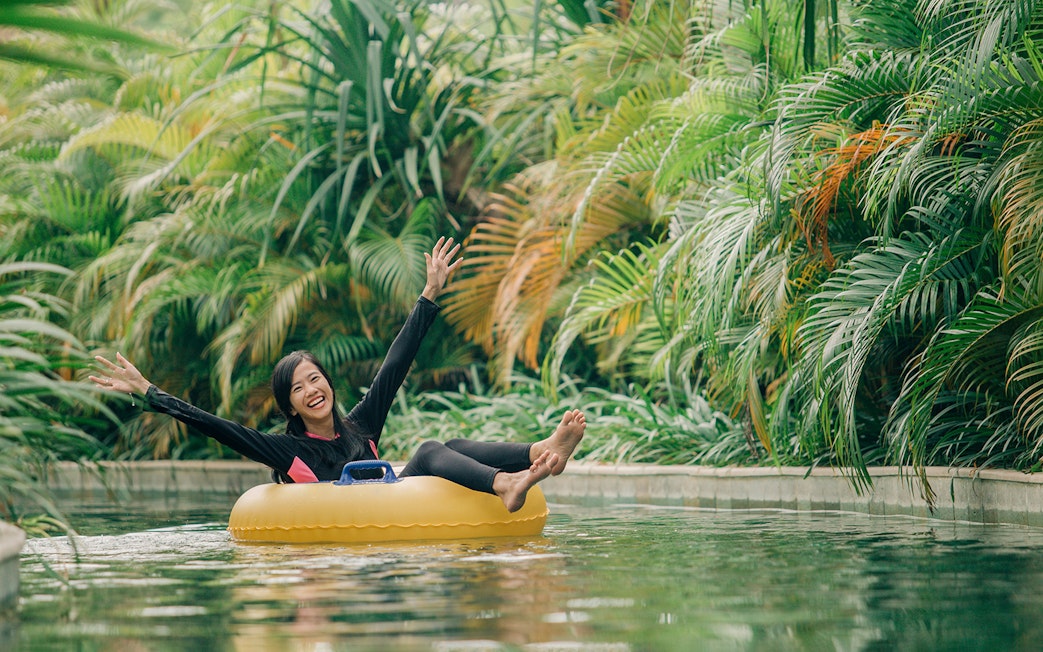 Girl floating on a ring in lazy river at Waterbom Bali surrounded by lush greenery.